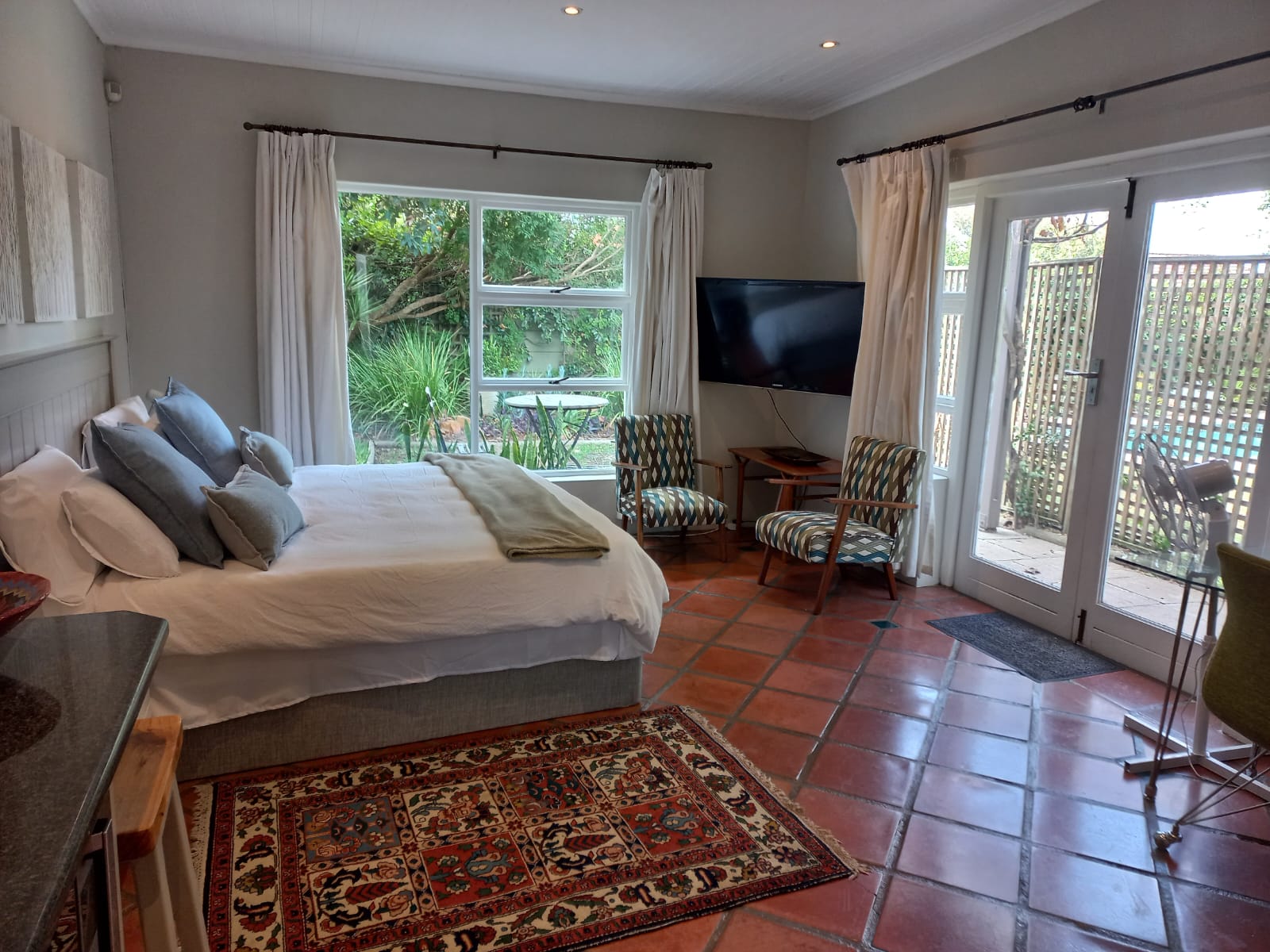 Spacious studio bedroom with king-sized bed, terracotta tiles, and garden view through double doors